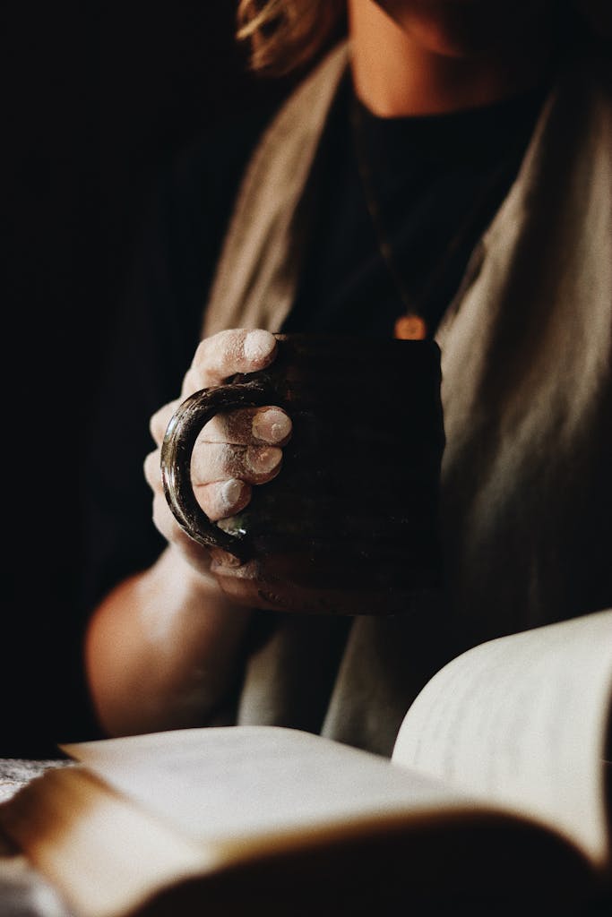 A woman with flour-dusted hands enjoying coffee while reading a book indoors.